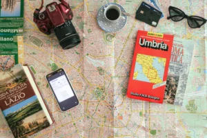 Flatlay zur Italienreiseplanung: Stadtplan von Mailand, Straßenkarte Umbrien, ein Flug-Boardingpass, Kamera und Reiseführer